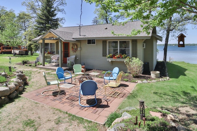 rear view of house with a patio area, a yard, an outdoor fire pit, roof with shingles, and a water view