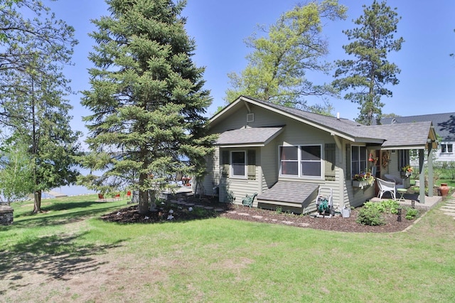 view of front facade featuring a front lawn, a patio, and a shingled roof