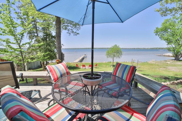 wooden terrace with outdoor dining area, a water view, and a lawn
