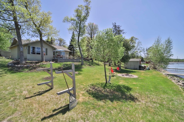 view of grassy yard featuring a fire pit, a water view, a shed, and an outbuilding