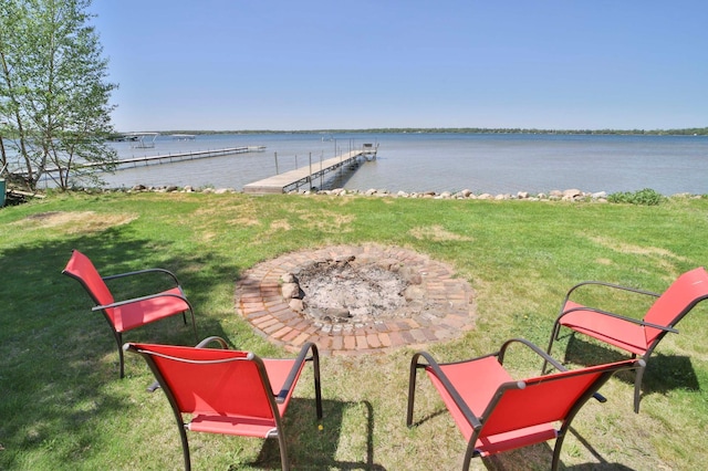 view of green lawn featuring a dock, a water view, and a fire pit