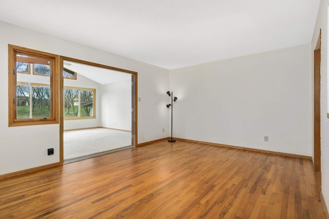 spare room featuring wood finished floors, lofted ceiling, and baseboards