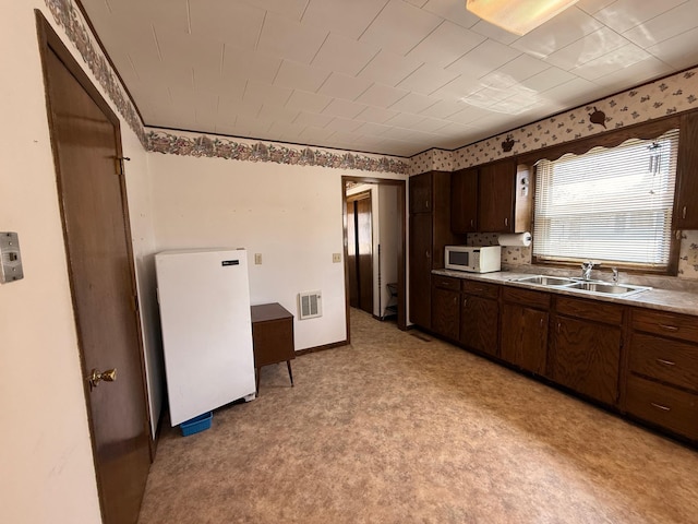 128 Munsterman St, Appleton, MN 56208 - kitchen with a sink, visible vents, dark brown cabinetry, white appliances, and light countertops