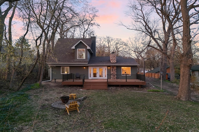 back of house at dusk with an outdoor fire pit, a wooden deck, a chimney, and a lawn