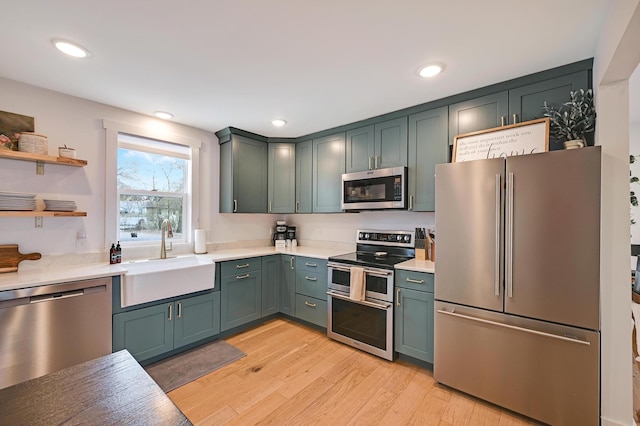 kitchen with a sink, open shelves, appliances with stainless steel finishes, light countertops, and light wood-style floors