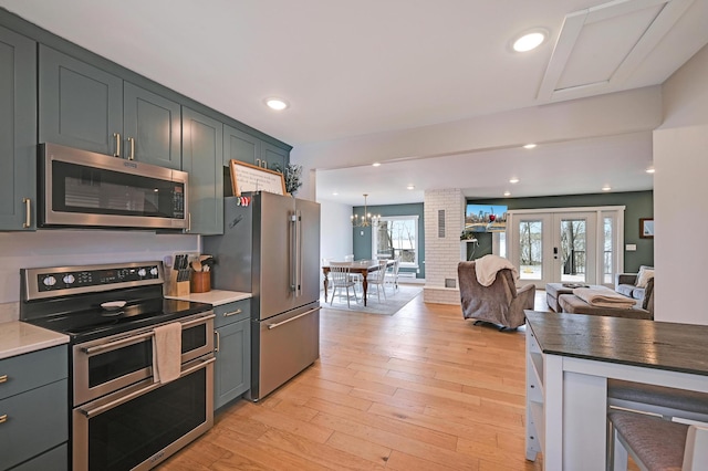 kitchen with an inviting chandelier, french doors, stainless steel appliances, open floor plan, and light wood-type flooring