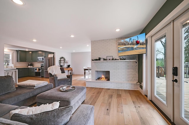 living area featuring light wood-style floors, baseboards, a brick fireplace, and recessed lighting