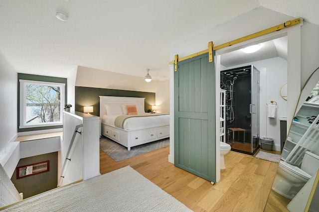 bedroom with vaulted ceiling, a barn door, and wood finished floors
