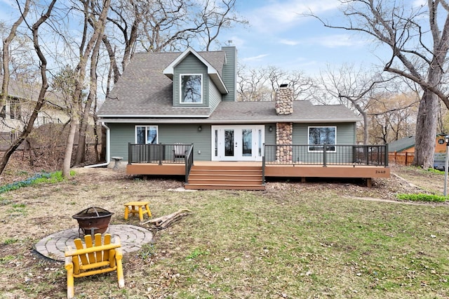 back of house with a chimney, a yard, a fire pit, a deck, and roof with shingles