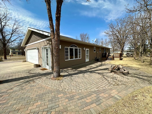 view of side of property featuring a fire pit, an attached garage, a wooden deck, and driveway