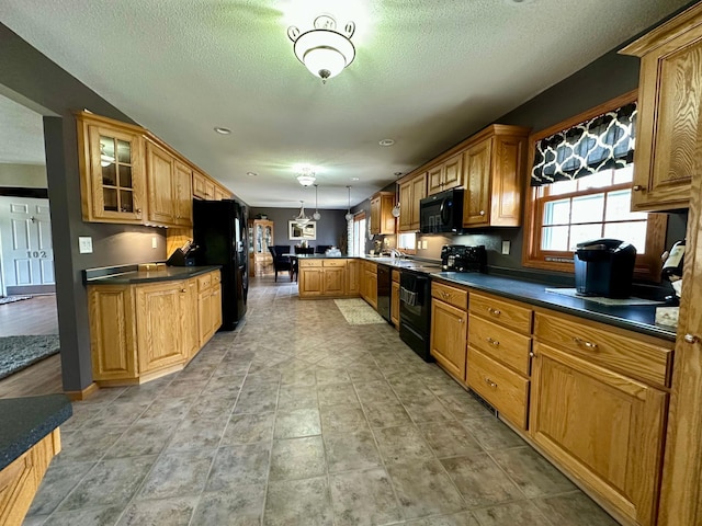 kitchen featuring dark countertops, black appliances, a peninsula, glass insert cabinets, and hanging light fixtures