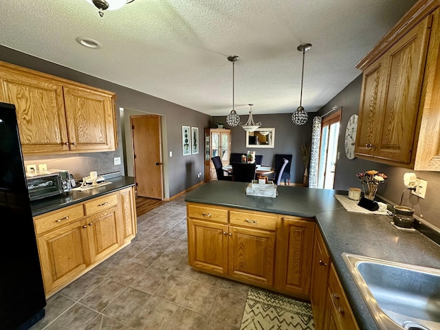 kitchen with dark countertops, a sink, a textured ceiling, a peninsula, and freestanding refrigerator