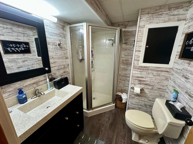 bathroom with a shower stall, wooden walls, wood finished floors, toilet, and vanity