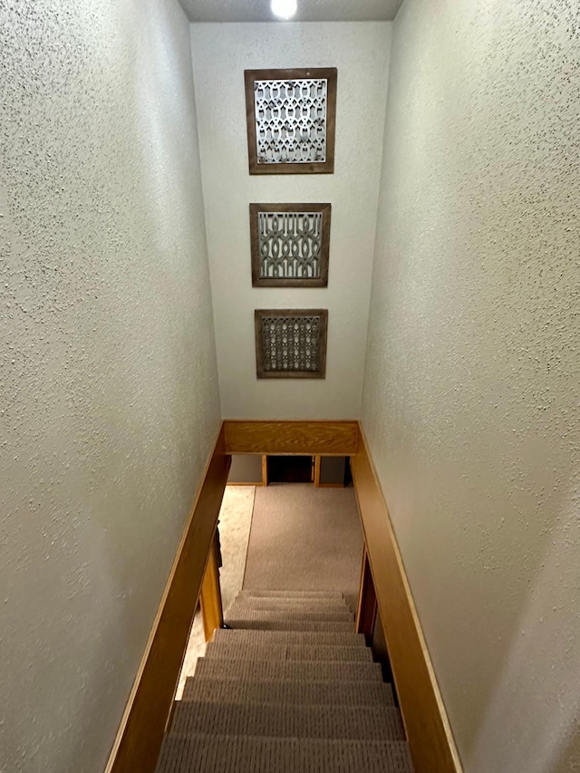 staircase featuring a textured wall and carpet