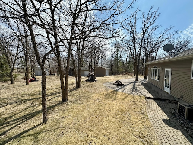 view of yard featuring central AC unit, a shed, an outbuilding, a patio, and an outdoor fire pit
