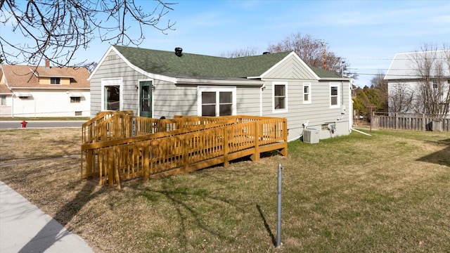 back of property with a wooden deck, a shingled roof, central AC unit, a lawn, and fence