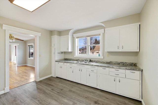 kitchen featuring light countertops, white cabinets, a sink, baseboards, and light wood-type flooring