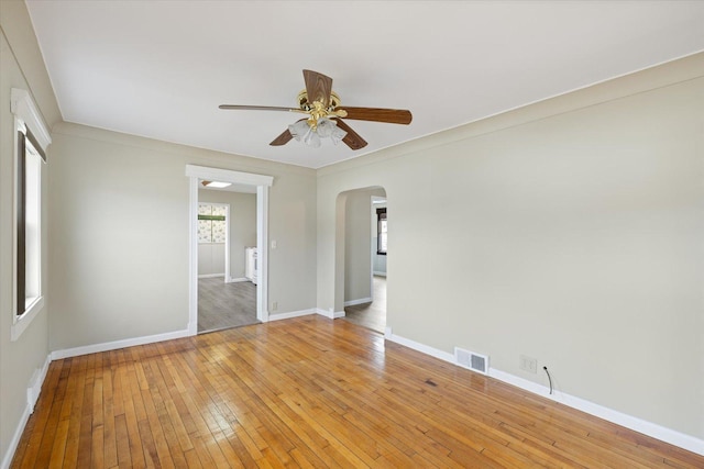 empty room with light wood-style floors, ceiling fan, visible vents, baseboards, and arched walkways