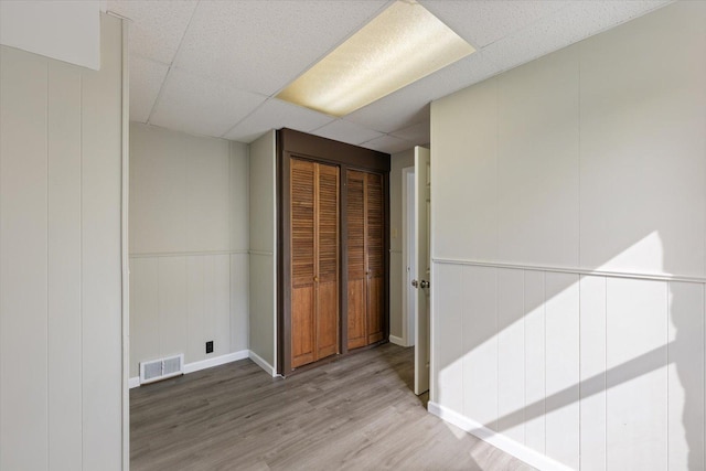 interior space with a closet, visible vents, a drop ceiling, and wood finished floors