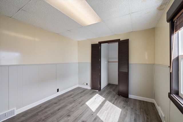 unfurnished bedroom featuring visible vents, wainscoting, a drop ceiling, and wood finished floors