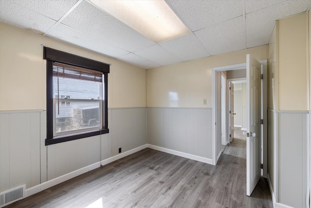 spare room featuring visible vents, wood finished floors, a wainscoted wall, and a drop ceiling