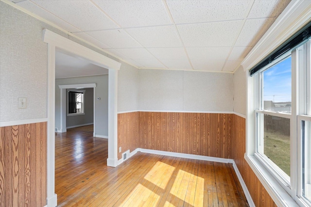 empty room featuring visible vents, a wainscoted wall, and wood-type flooring