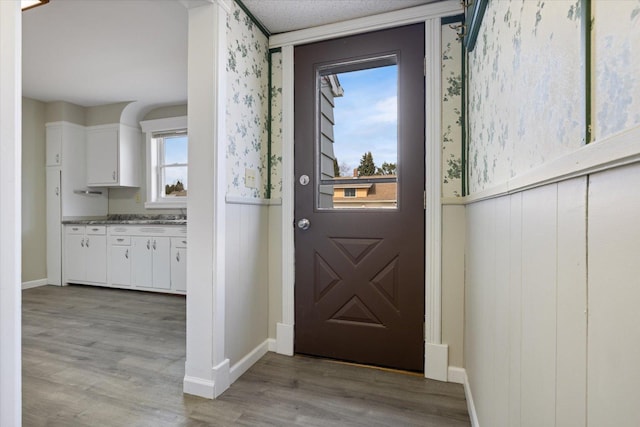 doorway to outside featuring light wood-style floors, wallpapered walls, and baseboards