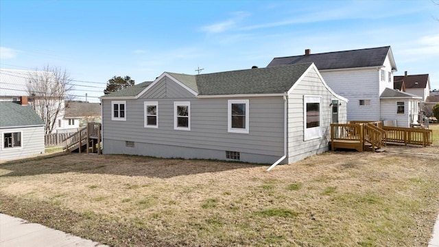 rear view of property with a lawn, roof with shingles, and a deck