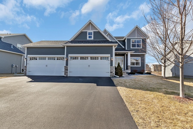craftsman-style home featuring an attached garage, a front yard, aphalt driveway, and stone siding