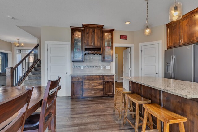 kitchen featuring hanging light fixtures, glass insert cabinets, stainless steel fridge, backsplash, and dark wood-style flooring
