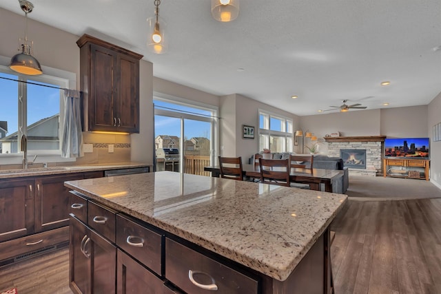 kitchen featuring a center island, a sink, dark wood finished floors, a ceiling fan, and a fireplace