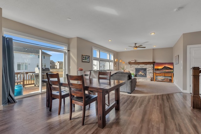 dining room featuring a stone fireplace, a ceiling fan, dark wood-type flooring, and baseboards
