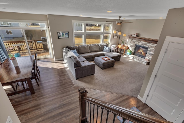 living room featuring a stone fireplace, wood finished floors, a ceiling fan, baseboards, and a textured ceiling