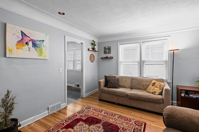 living room with a textured ceiling, visible vents, baseboards, and light wood finished floors