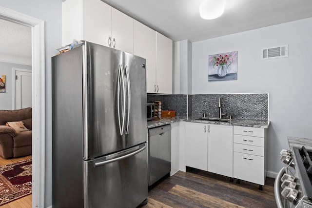 kitchen featuring a sink, stainless steel appliances, stone counters, dark wood-type flooring, and visible vents