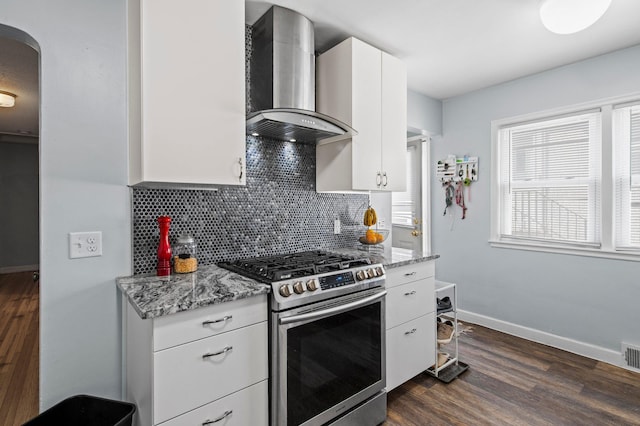 kitchen featuring stainless steel gas range oven, arched walkways, wall chimney exhaust hood, decorative backsplash, and dark wood-style floors