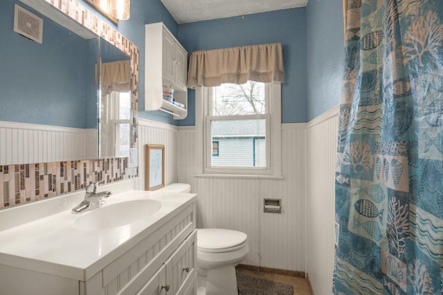 full bath with vanity, toilet, a wainscoted wall, and visible vents