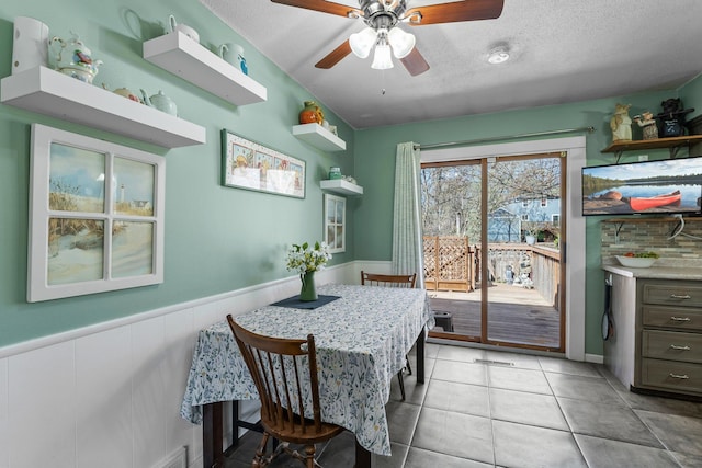 dining space with a textured ceiling, ceiling fan, wainscoting, and light tile patterned floors