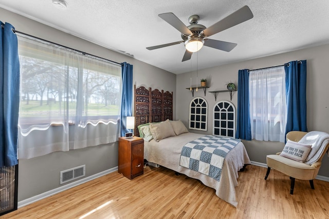 bedroom featuring baseboards, a textured ceiling, wood finished floors, and visible vents