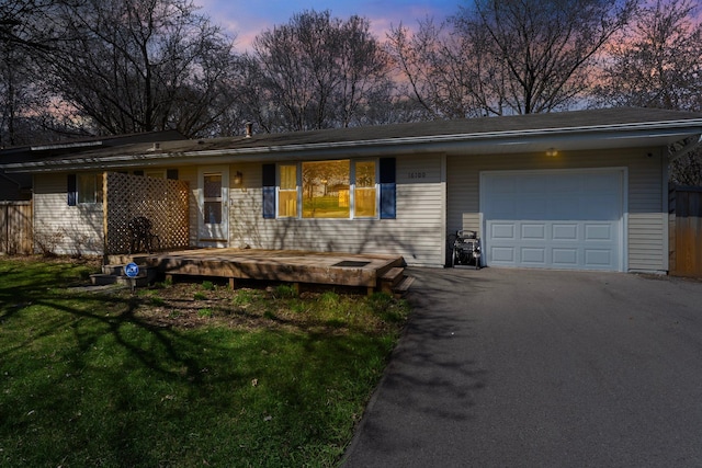 ranch-style house featuring fence, an attached garage, a front yard, and aphalt driveway