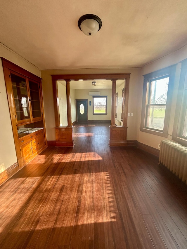 interior space featuring radiator, a healthy amount of sunlight, ornate columns, and dark wood-style flooring