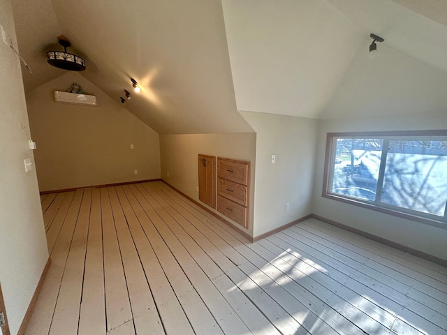 additional living space with light wood-style floors, vaulted ceiling, baseboards, and a wall unit AC