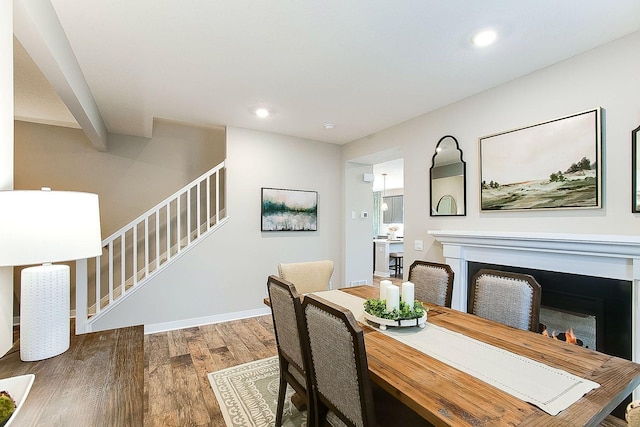 dining space with recessed lighting, stairs, wood finished floors, and a lit fireplace