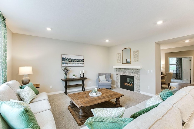 carpeted living area featuring baseboards, recessed lighting, and a stone fireplace