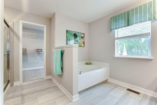 full bath featuring a shower stall, visible vents, baseboards, a garden tub, and a walk in closet