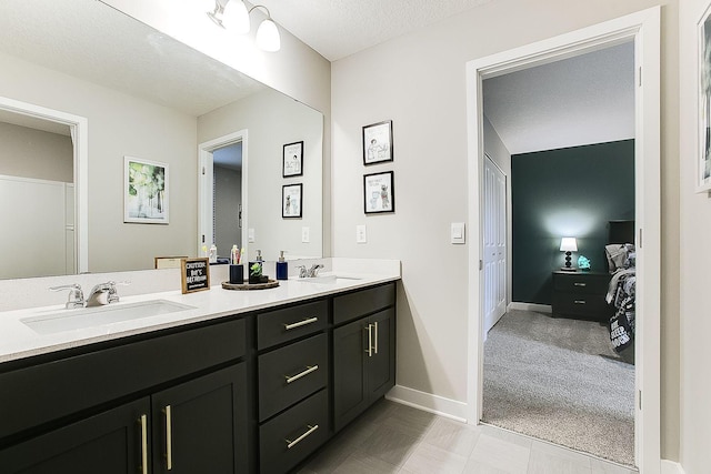 full bath featuring double vanity, a sink, a textured ceiling, and baseboards