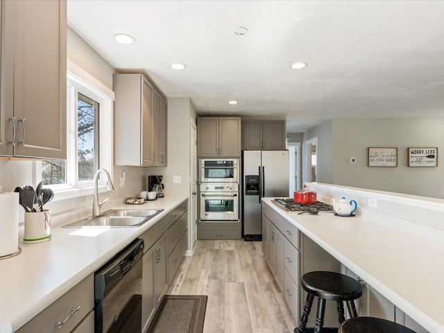 kitchen featuring a kitchen bar, light wood-type flooring, gray cabinets, a sink, and stainless steel appliances