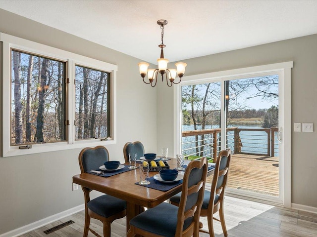 dining area featuring a water view, baseboards, light wood finished floors, and a notable chandelier