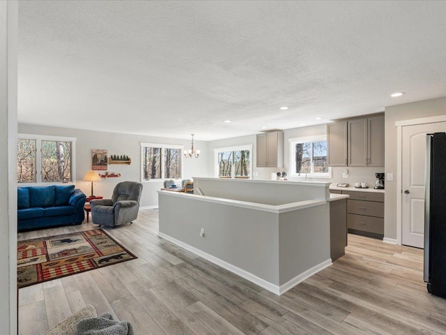 kitchen featuring an inviting chandelier, freestanding refrigerator, open floor plan, gray cabinets, and a textured ceiling
