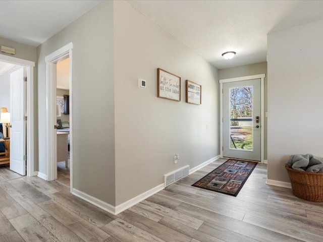 doorway with baseboards, visible vents, and wood finished floors